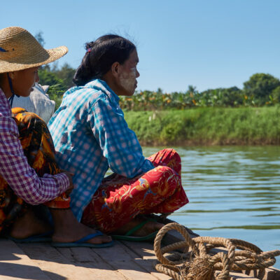 Two Burmese women sitting at the edge of a body of water.