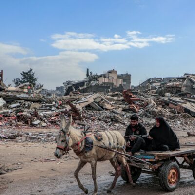 Two people on a horse and cart drive past destroyed buildings in Gaza, 2025.