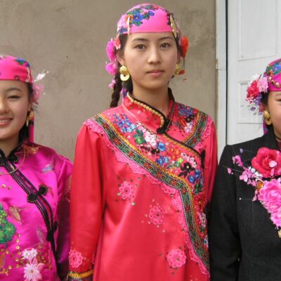 Three Dungan women standing side by side, posing for a photoshoot in traditional Dungan clothing, pink, red and black, 2004.